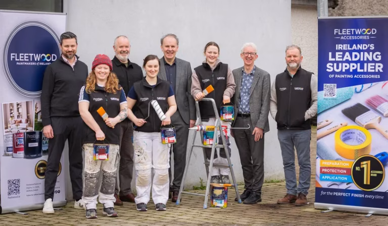 Group photo of eight people standing in front of Fleetwood signage, including three with paint rollers and accessories, conveying teamwork and professionalism.